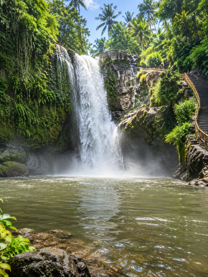 Une haute cascade tombant dans un bassin vert sous le soleil de la jungle de Bali