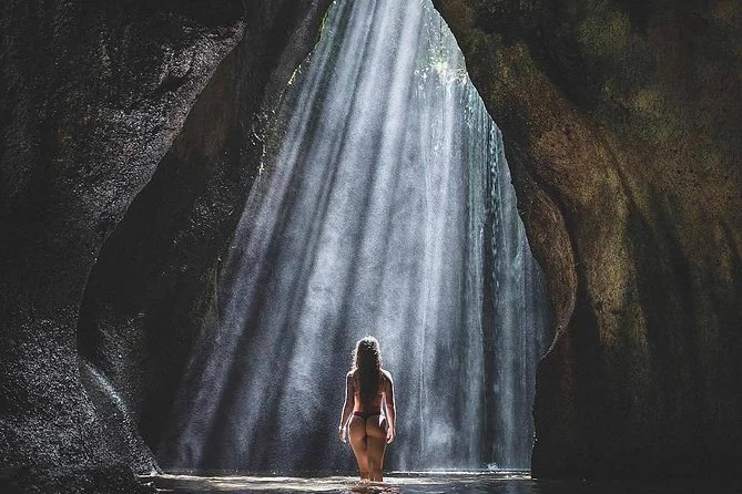 A shaft of sunlight falling through a narrow cave opening onto the waterfall at Tukad Cepung