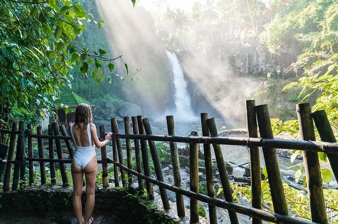 Una mujer de pie tras una valla de bambú junto a una cascada