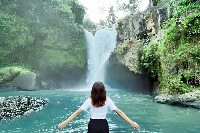 Una mujer con los brazos abiertos en una poza turquesa de una cascada